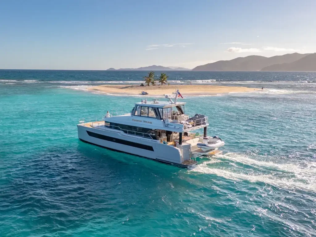 Power Catamaran Charters yacht cruising past a sandy Caribbean island in clear turquoise water.